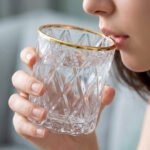 Close-up of a person drinking from an RCR-inspired crystal water glass featuring a textured diamond-cut pattern and a luxurious golden rim.