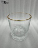 A close-up of a person drinking from a clear crystal glass with a gold-trimmed rim, alongside a studio shot of the glass showcasing a textured swirl pattern on the base.