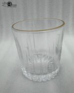 A close-up of a person holding a premium RCR-inspired crystal glass with a luxury gold rim and intricate geometric cut patterns.