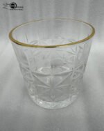 Close-up of a hand holding an RCR-inspired crystal water glass with a geometric starburst pattern and a decorative gold rim.