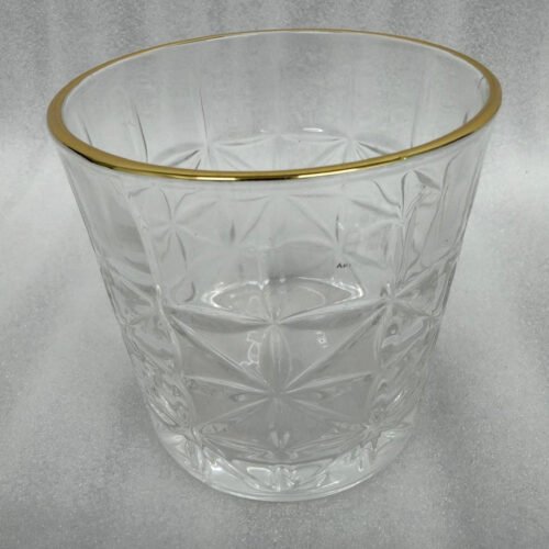 Close-up of a hand holding an RCR-inspired crystal water glass with a geometric starburst pattern and a decorative gold rim.