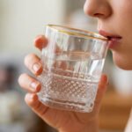 A close-up of a luxury crystal whiskey glass with a textured diamond-cut base and a thin golden rim, held by a person taking a drink.