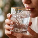 Close-up of a person drinking from an elegant crystal water glass featuring an embossed leaf pattern and a polished gold rim, highlighting the clarity and luxury design.