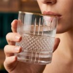 Close-up of a person holding a luxury crystal whiskey glass with an intricate diamond-cut pattern and a thin golden rim, filled with water and ice.