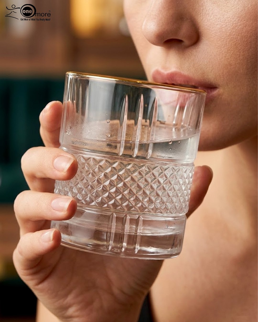 2 Close-up of a person holding a luxury crystal whiskey glass with an intricate diamond-cut pattern and a thin golden rim, filled with water and ice.