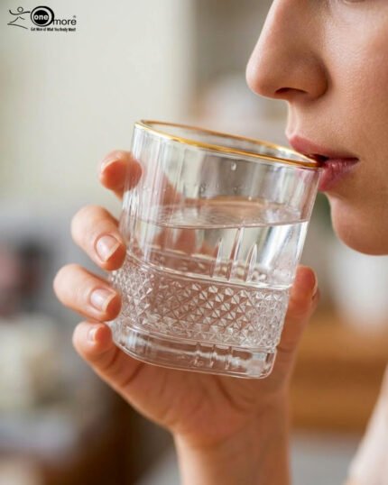 A close-up of a luxury crystal whiskey glass with a textured diamond-cut base and a thin golden rim, held by a person taking a drink.