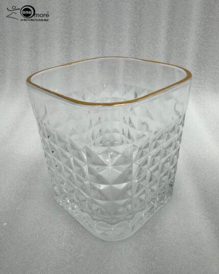 Close-up of a hand holding a diamond-textured crystal glass with a gold rim, filled with water, against a warm library background.