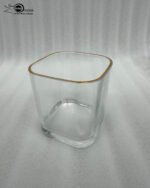 Close-up of a person holding a square-shaped crystal glass with a gold-painted rim, filled with clear water, showcasing the elegant transparency and luxury design.