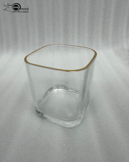 Close-up of a person holding a square-shaped crystal glass with a gold-painted rim, filled with clear water, showcasing the elegant transparency and luxury design.