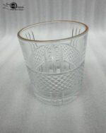 Close-up of a person holding a luxury crystal whiskey glass with an intricate diamond-cut pattern and a thin golden rim, filled with water and ice.