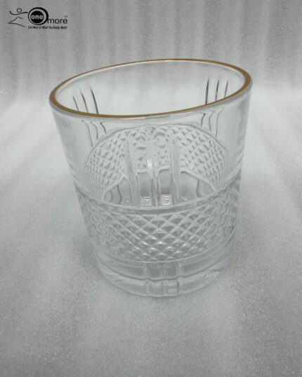 Close-up of a person holding a luxury crystal whiskey glass with an intricate diamond-cut pattern and a thin golden rim, filled with water and ice.