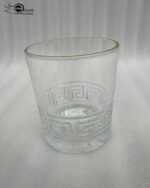 Close-up of a person drinking from a Versace-inspired crystal glass featuring an embossed Greek Key pattern and a luxury golden rim.