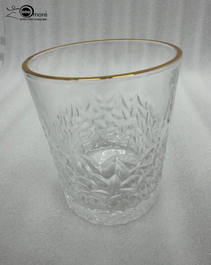 A close-up of a person holding a clear crystal water glass with a textured diamond pattern and a thin golden rim, showcasing the elegant light refraction through the water.