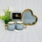 Five-piece stoneware couple set featuring two polka-dotted mugs with gold handles, a matching heart-shaped tray, and two white spoons, available in black, navy, sky blue, pink, and white.