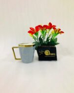 A luxury hexagonal ceramic coffee mug with gold marble veining, featuring a gold-plated square handle and rim, displayed next to a small potted plant with red flowers.