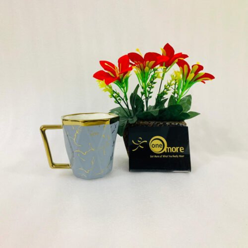 A luxury hexagonal ceramic coffee mug with gold marble veining, featuring a gold-plated square handle and rim, displayed next to a small potted plant with red flowers.