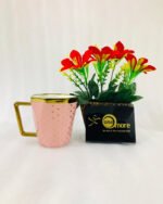 A modern hexagonal ceramic mug with gold polka dots and a gold handle, shown in two color options: blush pink and bright yellow, placed next to a small pot of red flowers.