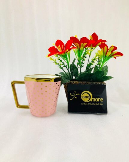 A modern hexagonal ceramic mug with gold polka dots and a gold handle, shown in two color options: blush pink and bright yellow, placed next to a small pot of red flowers.