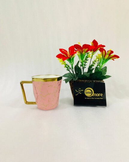 A luxury hexagonal ceramic coffee mug with gold marble veining, featuring a gold-plated square handle and rim, displayed next to a small potted plant with red flowers.