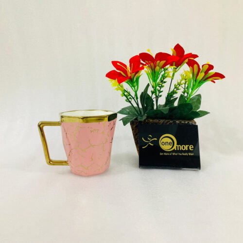 A luxury hexagonal ceramic coffee mug with gold marble veining, featuring a gold-plated square handle and rim, displayed next to a small potted plant with red flowers.