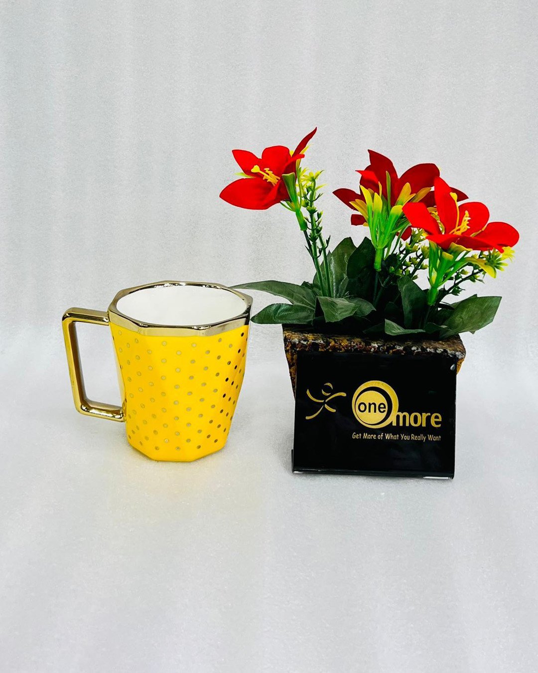 Yellow A modern hexagonal ceramic mug with gold polka dots and a gold handle, shown in two color options: blush pink and bright yellow, placed next to a small pot of red flowers.