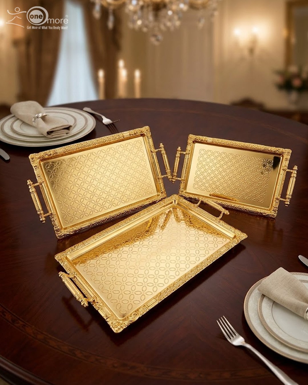 1 A luxury three-piece set of rectangular gold-plated stainless steel serving trays with intricate floral embossing and ornate vintage handles, displayed on a wooden dining table with elegant place settings.