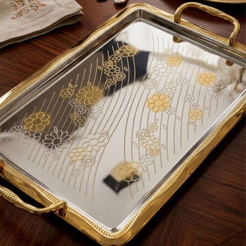 A set of three luxury Onemore brand stainless steel serving trays with gold-textured handles and borders, featuring etched floral patterns on a mirror-polished surface, displayed on a dark wooden dining table.