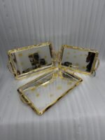 A set of three luxury Onemore brand stainless steel serving trays with gold-textured handles and borders, featuring etched floral patterns on a mirror-polished surface, displayed on a dark wooden dining table.