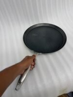 A professional-grade laser-etched non-stick stainless steel crepe pan with a textured honeycomb surface and ergonomic silver handle, shown on a kitchen counter and an induction cooktop.