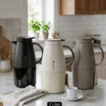 Three 2-liter luxury stainless steel thermal flasks in black, cream, and grey finishes with metallic handles, arranged on a white marble kitchen counter.