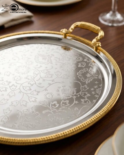 Set of three round silver stainless steel serving trays with floral etched patterns, gold rope borders, and ornate gold handles on a wooden dining table.