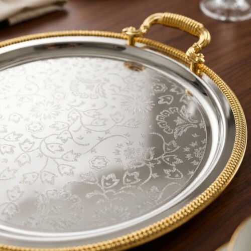 Set of three round silver stainless steel serving trays with floral etched patterns, gold rope borders, and ornate gold handles on a wooden dining table.
