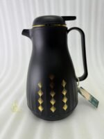 Two elegant 1-liter thermal carafes in matte black and slate blue with gold decorative patterns, displayed on a kitchen counter next to a coffee machine.