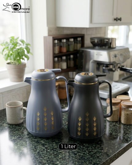 Two elegant 1-liter thermal carafes in matte black and slate blue with gold decorative patterns, displayed on a kitchen counter next to a coffee machine.
