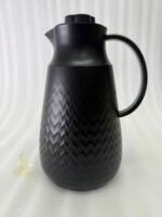 A 1-liter insulated thermal flask with a 3D diamond-patterned matte body, featuring a curved handle and a spout, shown in black and beige color options on a kitchen countertop.