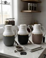 Three 1-liter Feenik thermal flasks in charcoal, taupe, and gray colors with gold trim on a marble kitchen countertop.