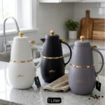 Three DayDays 1-liter luxury thermal flasks in white, black, and purple with gold accents displayed on a granite kitchen countertop.