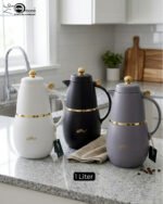 Three DayDays 1-liter luxury thermal flasks in white, black, and purple with gold accents displayed on a granite kitchen countertop.
