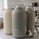 A collection of three 1-liter Feenik thermal flasks featuring a vertical ribbed design in beige, gray, and taupe on a white marble countertop.