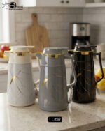 Three elegant 1-liter vacuum flasks in black, grey, and cream colors, featuring a golden Kintsugi-inspired marble pattern on a kitchen countertop.
