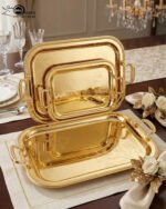 Three-piece set of luxury gold-plated stainless steel serving trays with intricate floral engravings and textured handles, displayed on a formal dining table.