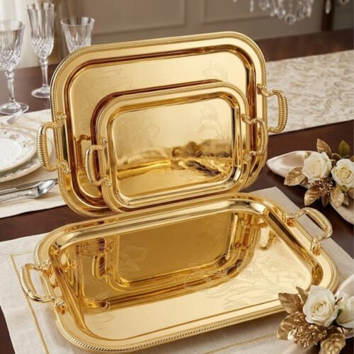 Three-piece set of luxury gold-plated stainless steel serving trays with intricate floral engravings and textured handles, displayed on a formal dining table.