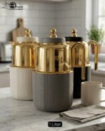 Three luxury 1-liter thermal flasks in white, grey, and black with polished gold tops and ribbed textured bases on a marble kitchen counter.