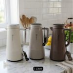 A trio of Feenik 1-liter thermal vacuum flasks in cream, sand grey, and mocha colors, displayed on a marble kitchen countertop.