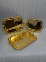 Three-piece set of luxury gold-plated stainless steel serving trays with intricate floral engravings and textured handles, displayed on a formal dining table.