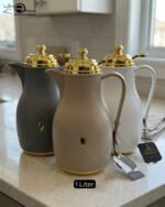 Three 1-liter thermal flasks in grey, beige, and white featuring matte finishes, elegant gold lids, and ergonomic handles on a marble countertop.