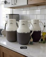 Three 1-liter modern vacuum flasks with cream-colored tops and ribbed bases in brown, grey, and beige, displayed on a white marble kitchen countertop.