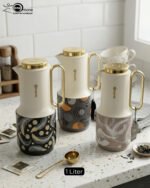 A trio of Feenik 1-liter luxury thermal flasks in cream with gold handles and lids, featuring three different artistic patterns on the base, displayed on a white marble kitchen counter.