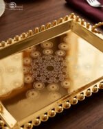 Add a touch of regal sophistication to your hosting with this exquisite 3-piece gold-plated stainless steel tray set. Featuring an intricate, laser-etched mandala design at the center and a decorative beaded "pearl" border, these trays blend traditional artistry with modern durability. The high-polish mirror finish reflects light beautifully, making them a stunning centerpiece for dining tables, coffee tables, or vanity displays. Whether you are serving refreshments to guests or organizing luxury accessories, this nesting set provides a versatile and opulent solution for any home. Key Features Premium Craftsmanship: Constructed from high-grade stainless steel with a brilliant gold-toned finish for long-lasting shine and rust resistance. Intricate Mandala Art: Each tray features a precision-etched geometric mandala pattern that adds a unique, artisanal feel to the collection. Ornate Beaded Edges: The scalloped rims are adorned with gold bead detailing, providing a secure grip and a sophisticated aesthetic. Versatile Set of Three: Includes small, medium, and large sizes that nest together for easy storage or can be used separately for multi-course serving. Multi-Purpose Decor: Ideal for serving appetizers, tea, and desserts, or used as a decorative base for candles, perfumes, and floral arrangements.