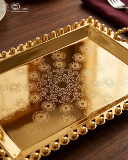 Add a touch of regal sophistication to your hosting with this exquisite 3-piece gold-plated stainless steel tray set. Featuring an intricate, laser-etched mandala design at the center and a decorative beaded "pearl" border, these trays blend traditional artistry with modern durability. The high-polish mirror finish reflects light beautifully, making them a stunning centerpiece for dining tables, coffee tables, or vanity displays. Whether you are serving refreshments to guests or organizing luxury accessories, this nesting set provides a versatile and opulent solution for any home. Key Features Premium Craftsmanship: Constructed from high-grade stainless steel with a brilliant gold-toned finish for long-lasting shine and rust resistance. Intricate Mandala Art: Each tray features a precision-etched geometric mandala pattern that adds a unique, artisanal feel to the collection. Ornate Beaded Edges: The scalloped rims are adorned with gold bead detailing, providing a secure grip and a sophisticated aesthetic. Versatile Set of Three: Includes small, medium, and large sizes that nest together for easy storage or can be used separately for multi-course serving. Multi-Purpose Decor: Ideal for serving appetizers, tea, and desserts, or used as a decorative base for candles, perfumes, and floral arrangements.